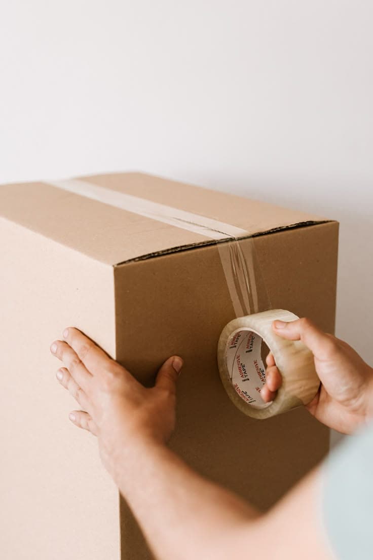 Manos sellando una caja de mudanza con cinta adhesiva
